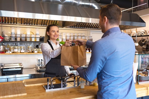 kitchen worker handing a paper bag to a customer